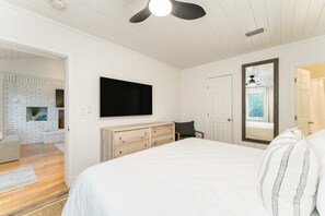 Ein Schlafzimmer mit einem Bett, einem Schminktisch, einem Fernseher und einem Kamin aus weißem Mauerwerk.