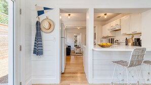 A modern kitchen with white cabinetry, a central island with bar stools, and a view into the dining area. - Twin Fin by Avantstay Walk to the Beach - Chic 30A Retreat (Panama City Beach)