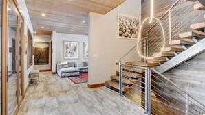 Ein modernes Interieur mit einer Holztreppe, einer Wohnbereits mit einer Couch und einem Flur, der zu einem Schlafzimmer führt.