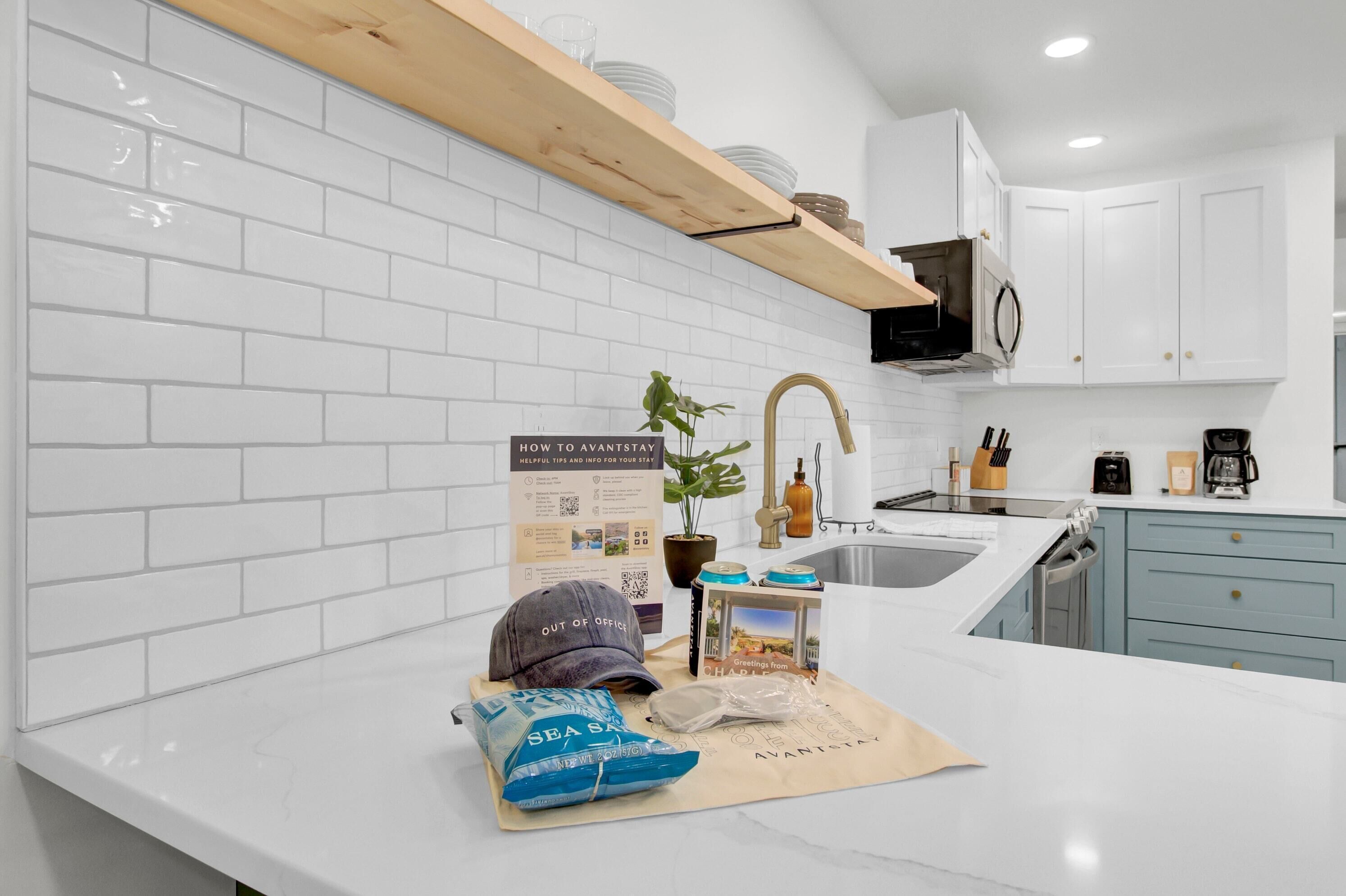 A modern kitchen with white subway tiles, a wooden shelf, and a sign about staying at the hotel.