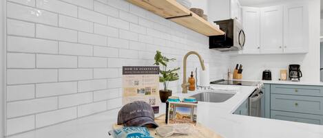 A modern kitchen with white subway tiles, a wooden shelf, and a sign about staying at the hotel.