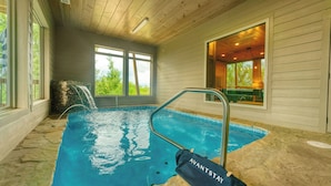Ein Hallenbad mit klarem Wasser, einer Steinwand und einer Holzbalkendecke.