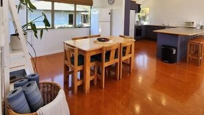 A spacious kitchen with a dining area, wooden furniture, and a large window. - Easy Days - Ideal 2 wing set up, quiet street, central, 5min walk to the beach (Hahei)