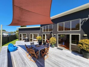 Een modern huis met twee verdiepingen, een terras, zitplaatsen buiten en grote ramen.