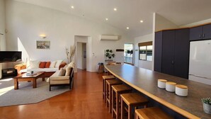 A modern kitchen with a long island counter, wooden stools, and a refrigerator. - Easy Days - Ideal 2 wing set up, quiet street, central, 5min walk to the beach (Hahei)