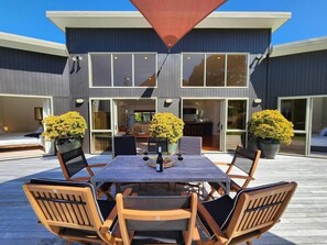 Een modern huis met een terras, voorzien van een eettafel en stoelen, omringd door grote ramen en potplanten.