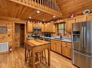 A wooden cabin interior with a kitchen featuring a stainless steel refrigerator, a microwave, and a sink.