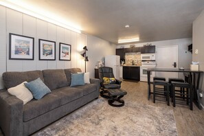 A modern living room with a gray sofa, a black chair, and a small dining area with a table and stools.