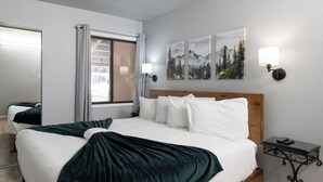 Ein Hotelzimmer mit einem großen Bett, einem Nachttisch, einem Fenster mit Vorhängen und Wandbildern.