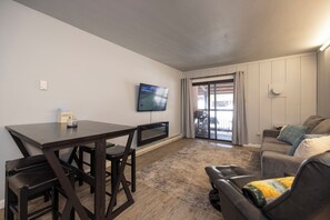 A modern living room with a flat-screen TV, a dining table, and a sofa.