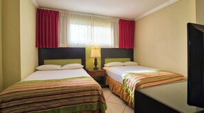 Two single beds with striped bedspreads, a flat-screen TV, and a bedside table with a lamp.