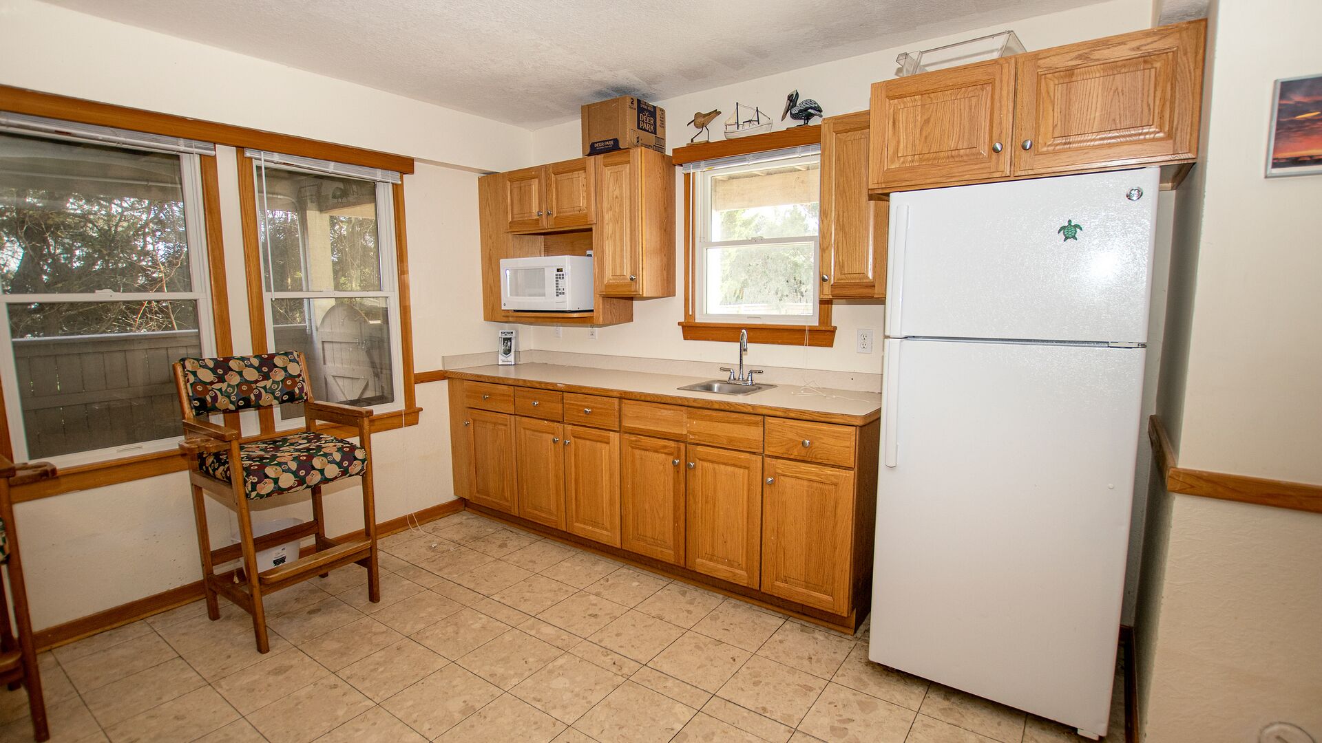 Una cocina con armarios de madera, un refrigerador blanco, un microondas y una ventana con una silla delante.