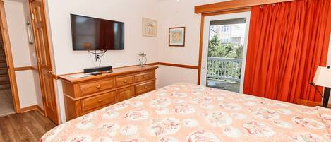Un dormitorio con una cama grande, televisor montado en la pared, cómoda y balcón con cortinas rojas.