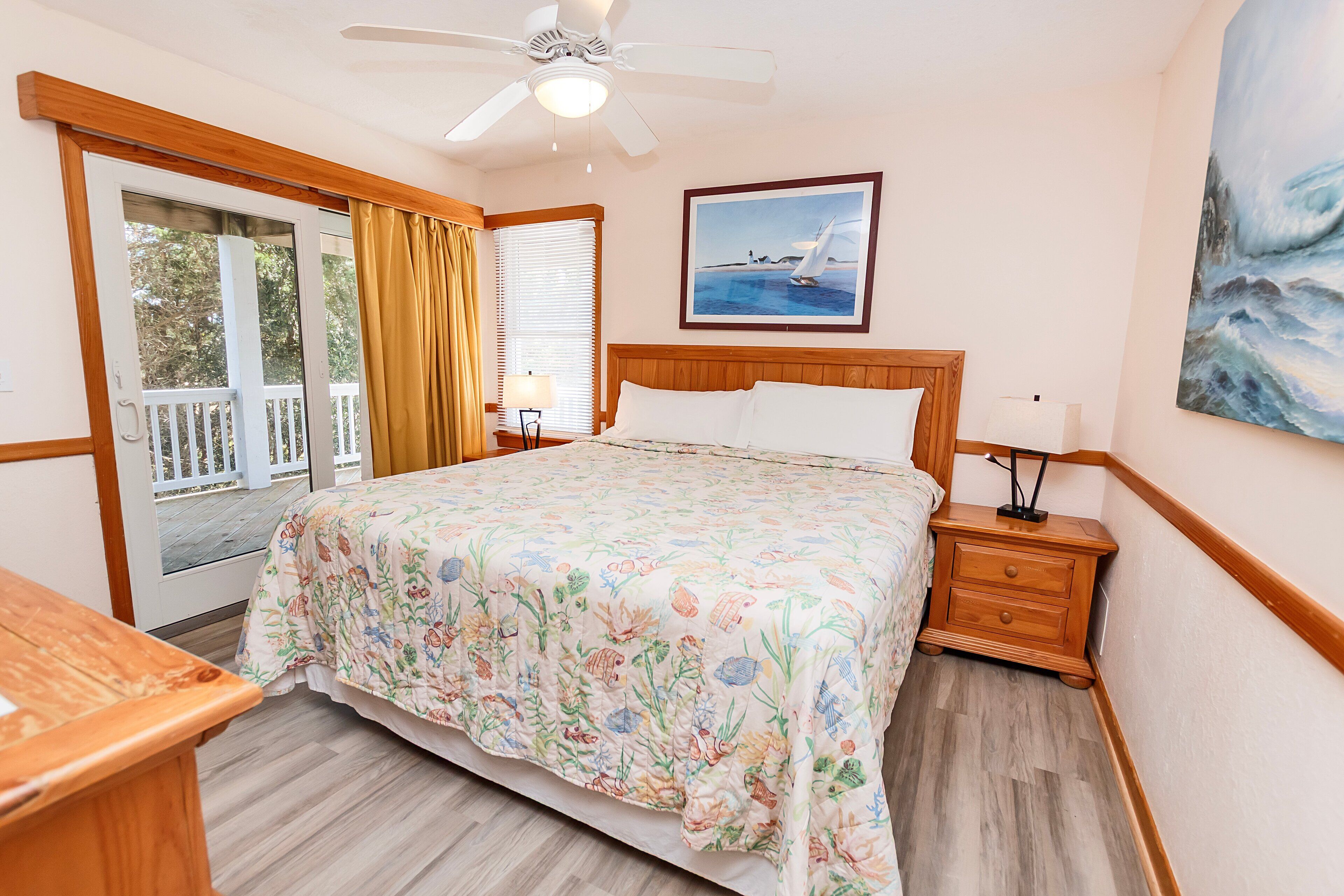A bedroom with a bed, a nightstand, a ceiling fan, a window with curtains, and a painting on the wall.
