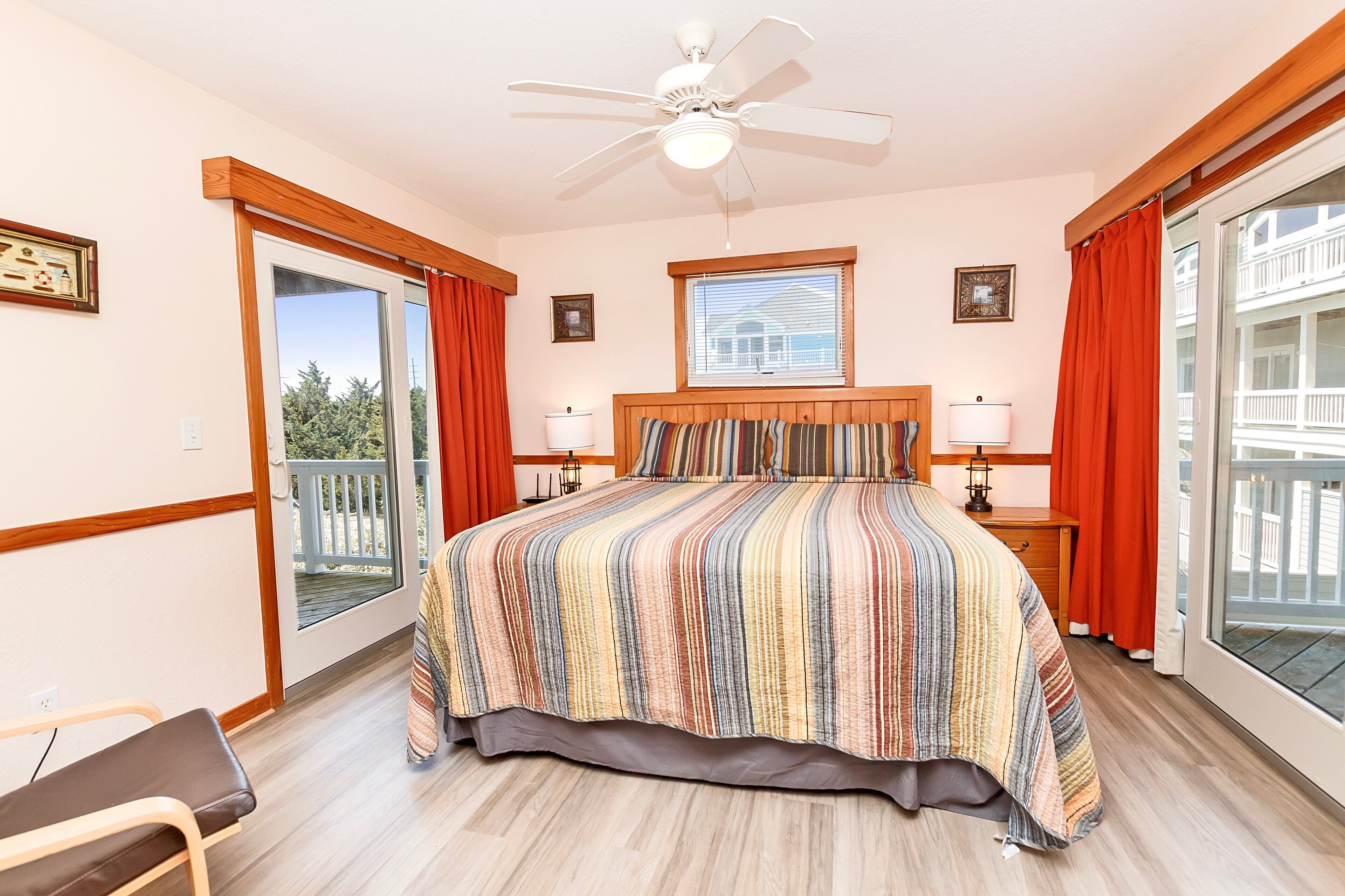 A bedroom with a large bed, a ceiling fan, a window with blinds, and a view of a balcony.