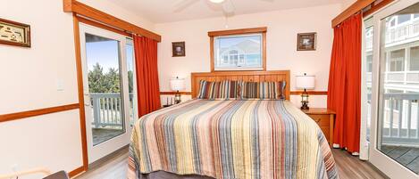 A bedroom with a large bed, a ceiling fan, a window with blinds, and a view of a balcony.