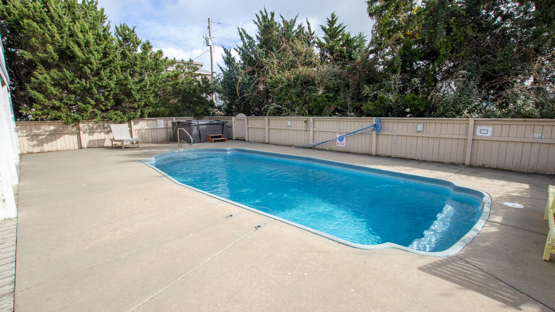 A rectangular swimming pool with a blue edge, surrounded by a concrete deck and a wooden fence.