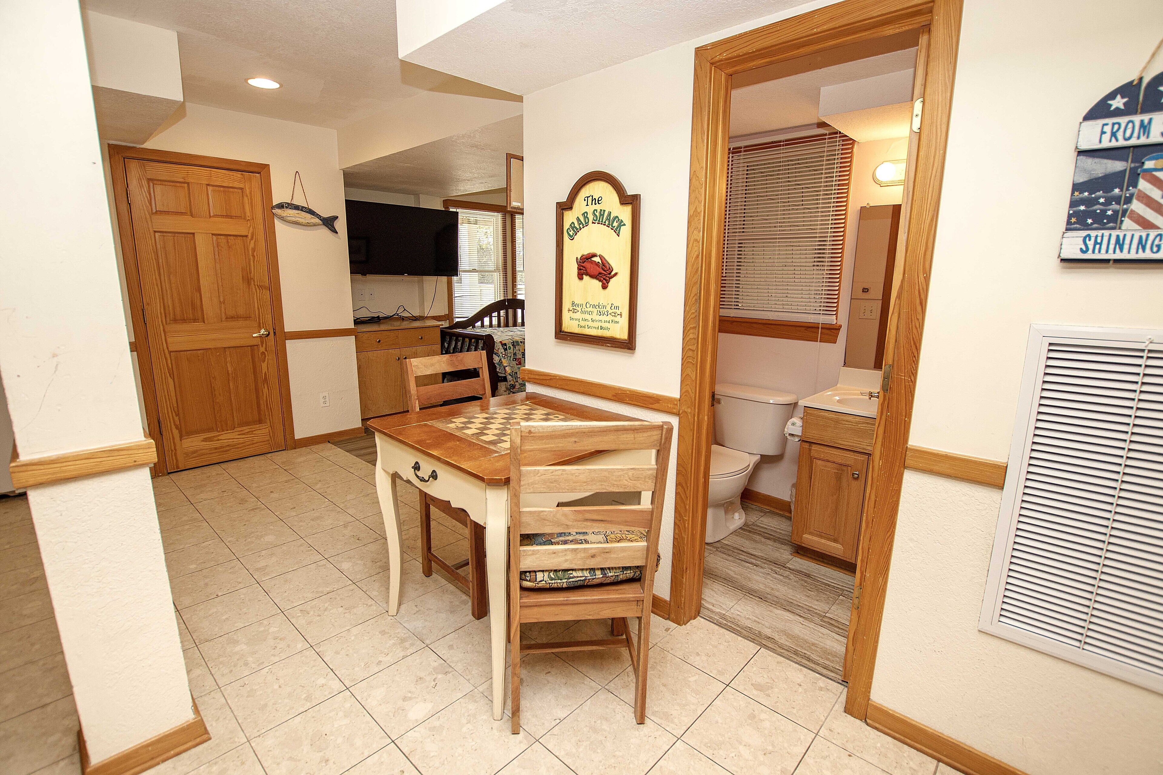 Une cuisine compacte avec des meubles en bois, une table à manger avec des chaises, un téléviseur et un panneau encadré accroché au mur.