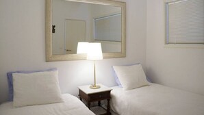 Een hotelkamer met twee bedden, een grote spiegel, een nachtkastje met lamp en een raam met zonwering.