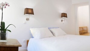 Een slaapkamer met een bed, twee wandlampen, een potplant en een houten bankje.