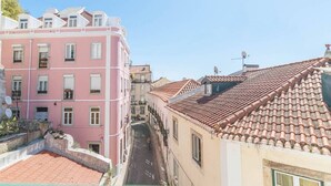 A narrow street flanked by buildings with terracotta roofs and a pink building with balconies. - Cozy Two Bedroom Apt in Central Alfama | With A/c by Lisbeyond (Lisboa)