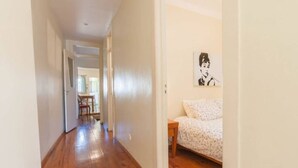 A narrow hallway with wooden flooring leading to a bedroom with a bed and a small table. - Cozy Two Bedroom Apt in Central Alfama | With A/c by Lisbeyond (Lisboa)