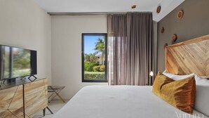 Une chambre d’hôtel moderne avec un grand lit, un téléviseur à écran plat posé sur un meuble en bois, et une vue sur un jardin par la fenêtre.