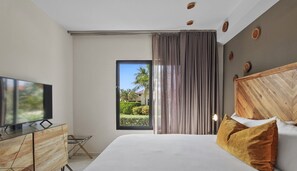 A modern hotel room with a large bed, a flat-screen TV on a wooden cabinet, and a view of a garden through a window.
