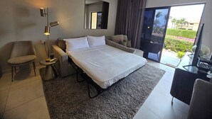 A modern hotel room with a large bed, a sofa, a chair, a desk, and a view of the outdoors.