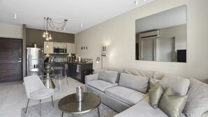 A modern living room with a grey sofa, a coffee table, and a dining area with chairs.