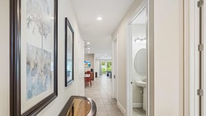 Un couloir orné de tableaux encadrés, avec un banc en bois, et une vue sur une salle à manger et une salle de bain.