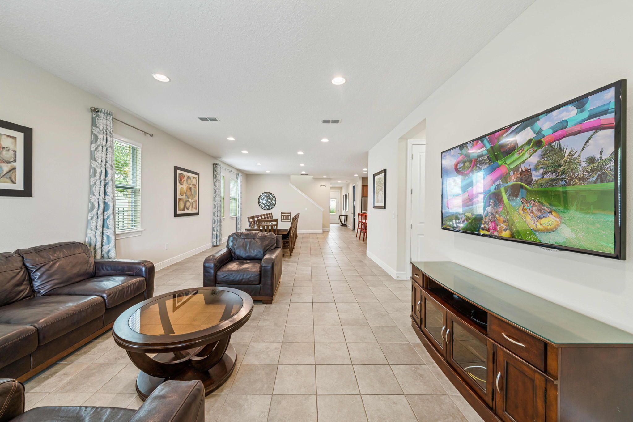 A spacious living room with a large flat-screen TV, leather sofas, a coffee table, and a dining area with chairs and a table.