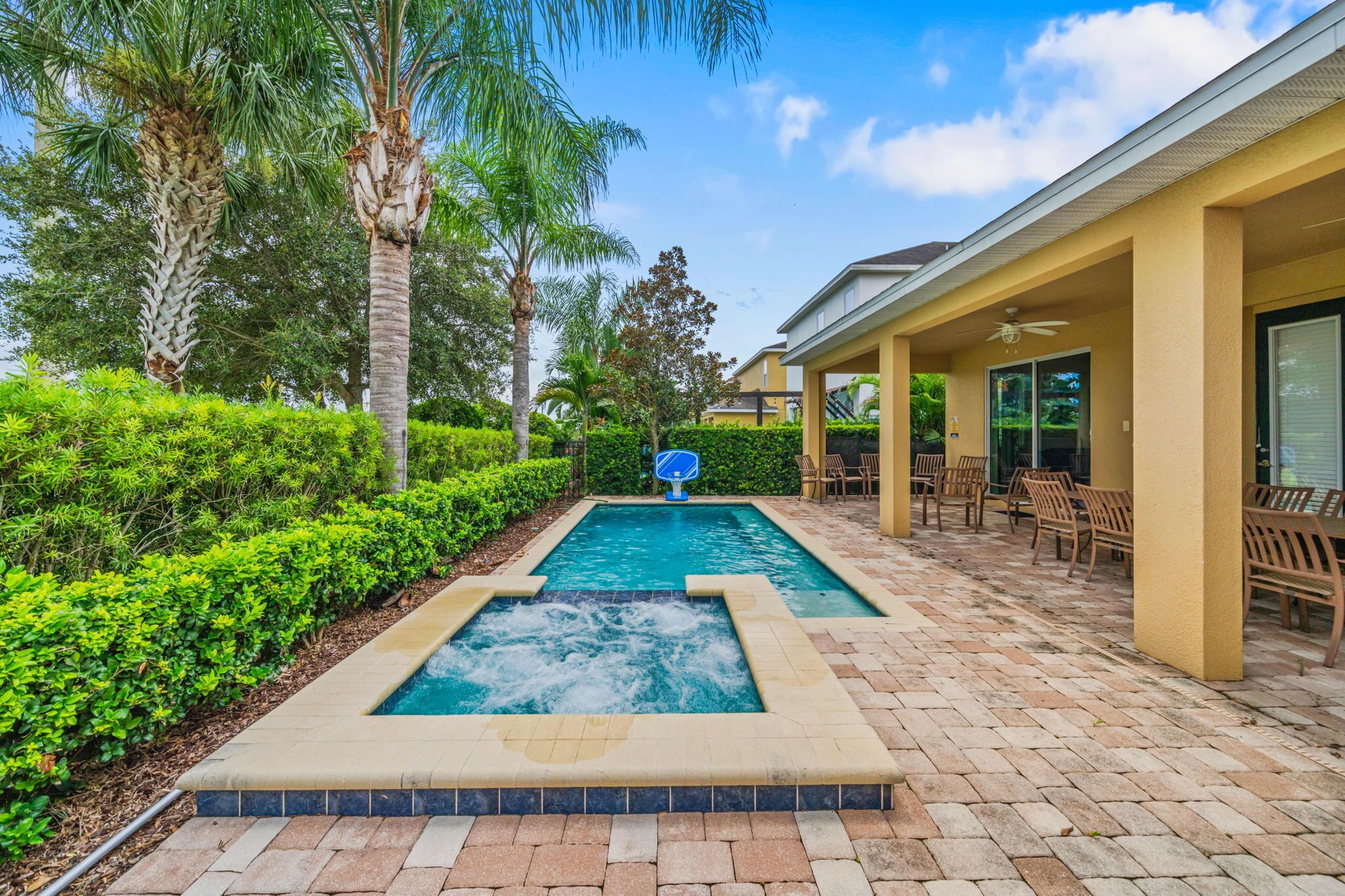 Une piscine avec un jacuzzi, entourée de palmiers et dotée d’un patio avec des chaises et un espace dédié à la bronzette.