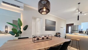 A modern kitchen with a built-in refrigerator, a dining area with a wooden table and chairs, and a hanging light fixture.