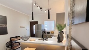 A modern kitchen with a central island, bar stools, a refrigerator, and a hanging light fixture.