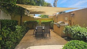 A patio with a table and chairs, a grill, and a shaded area.
