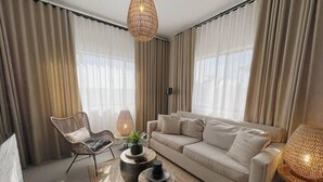 En moderne stue med en beige sofa, en fletstol og et rundt sofabord.