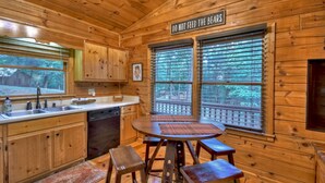 A wooden cabin interior with a kitchen area, a dining table with stools, and a sign that reads "DO NOT FEED THE BEARS". - Cozy Retreat with Hot Tub, Firepit & Fireplace! - Bearfoot Ridge (Blue Ridge)
