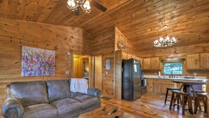 A cozy log cabin interior with a leather sofa, wooden dining table, and a chandelier. - Cozy Retreat with Hot Tub, Firepit & Fireplace! - Bearfoot Ridge (Blue Ridge)