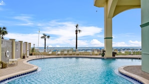 Zona de piscina con vista a la playa, palmeras y cielo despejado.