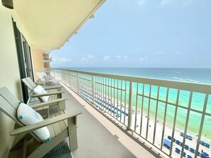 Een balkon met uitzicht op het strand, ligbedden en parasols.
