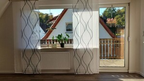 Une pièce dotée d’une grande fenêtre, d’un radiateur et d’une plante suspendue.