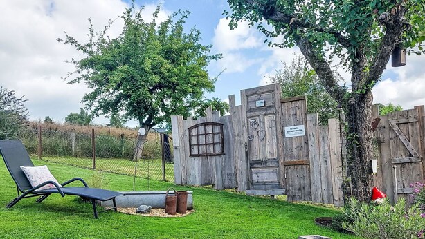 Un espace extérieur rustique agrémenté d’une clôture en bois, d’un portail en métal, d’un banc et d’un petit arbre.