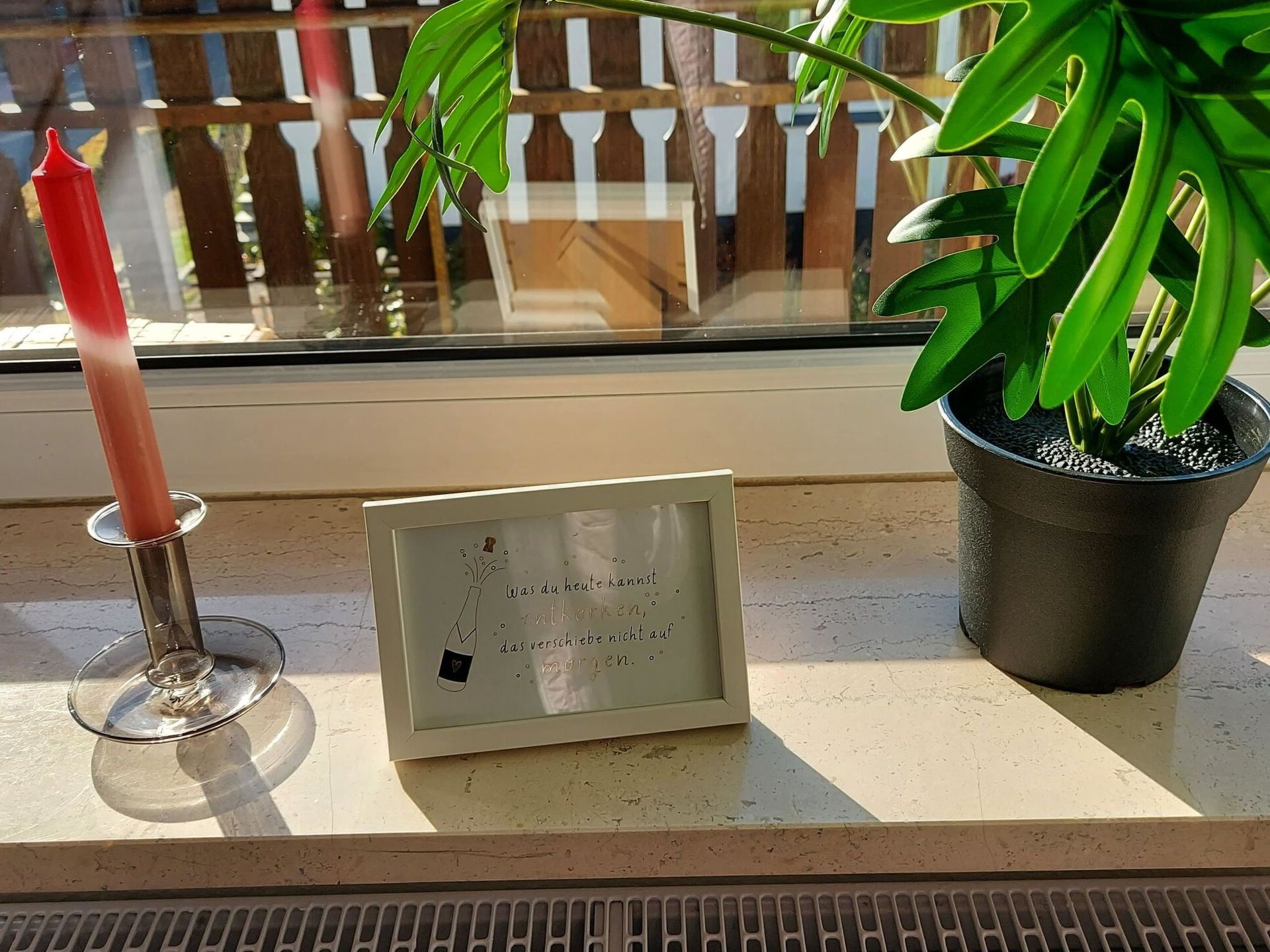A candle, a framed quote, and a potted plant on a windowsill.