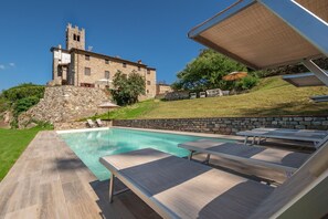 Una piscina con lettini, un muro in pietra e una vista su un edificio storico sullo sfondo.