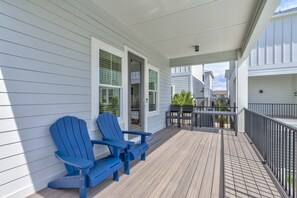 Une terrasse en bois avec deux chaises Adirondack bleues, une rambarde et une porte donnant sur un espace abrité.