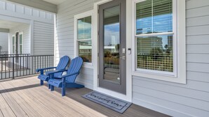 Eine Veranda mit zwei Adirondack-Stühlen, einer grauen Tür und einem Fenster mit Jalousien.