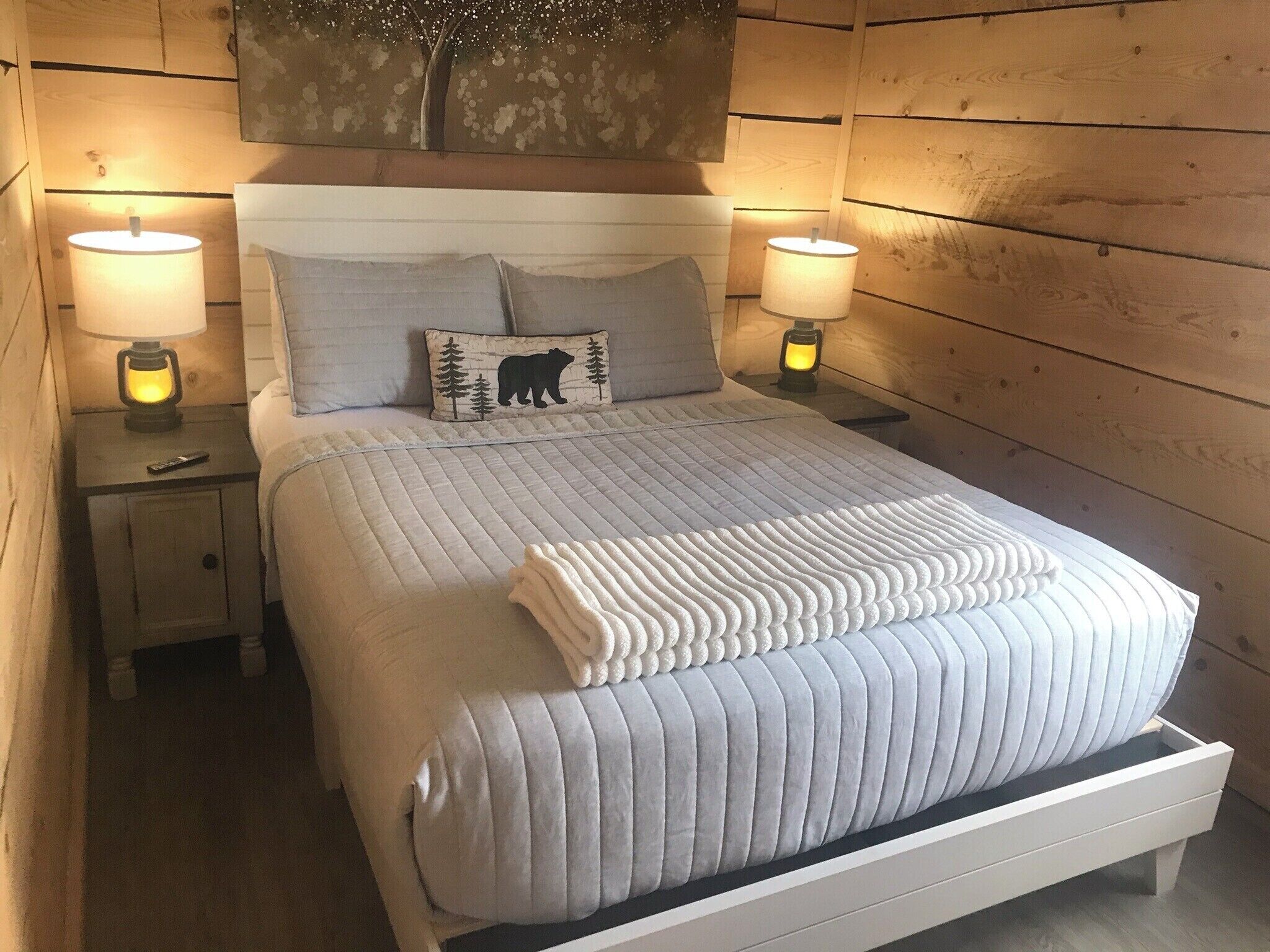 A neatly made bed with a quilted duvet, two bedside lamps, and a nightstand with a remote control.