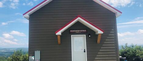 A small cabin labeled "MOUNTAINTOP RETREAT CABIN #1" with a white door, a red roof, and a gravel driveway.