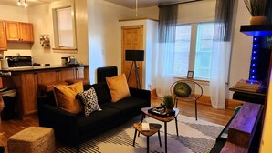 A cozy living room with a black sofa, a small coffee table, and a wooden floor.